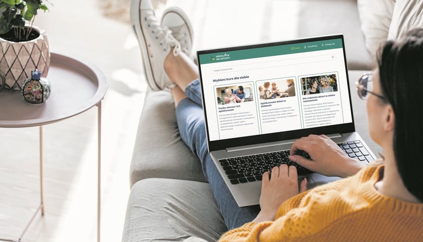 Kobieta siedzi na kanapie, na kolanach trzyma laptop i ma na wyświetlaczu portal www.wroclawsieszczepi.pl