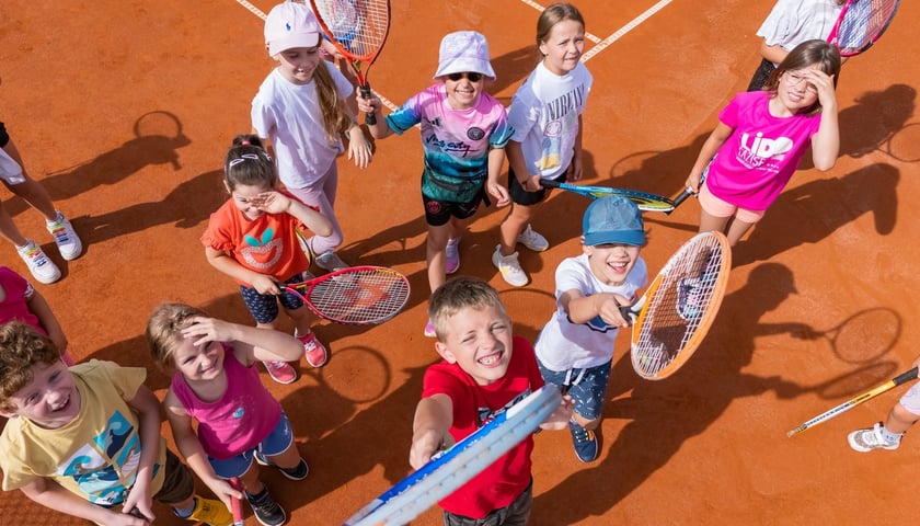 Grupa dzieci na boisku tenisowym z rakietami