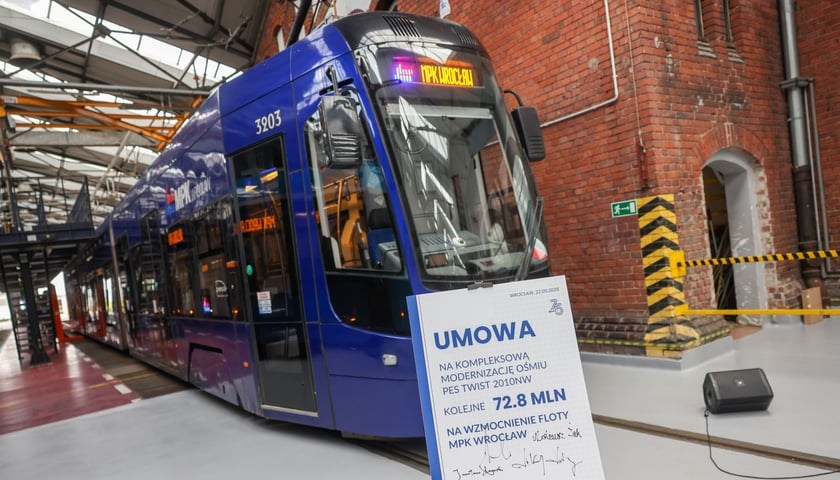 Tramwaj Pesa 2010NW na zajezdni Gaj, a przed nim tablica symbolizująca umowę na modernizację tych pojazdów