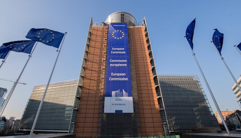 Budynek Komisji Europejskiej w Brukseli. Na tle niebieskiego nieba powiewają flagi Uni Europejskiej