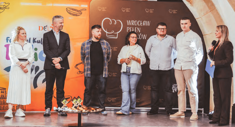7 osób na tle ścianki „Festiwal Kulinarny Delicje 2026” i „Wrocław Pełen Smaków”. Wśród nich jury: Marcin Jenczelewski (Piwnica Świdnicka), Joanna Komorowska (blogerka), Tomasz Tyc (współorganizator) oraz Ivan Svyshchuk (szef Valley)