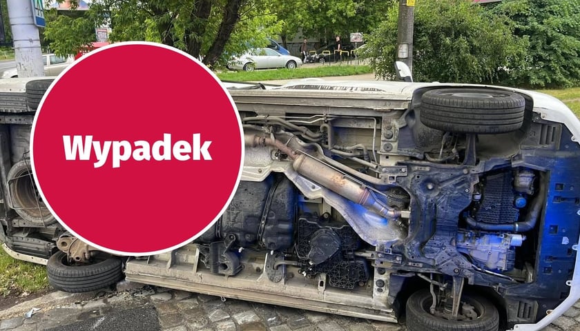 w tle: samochód leżący na boku; w kółku: napis "wypadek" na czerwonym tle