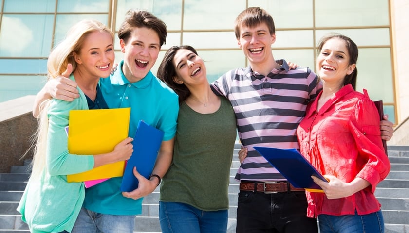 Na zdjęciu grupa młodych uśmiechniętych ludzi w wieku studenckim