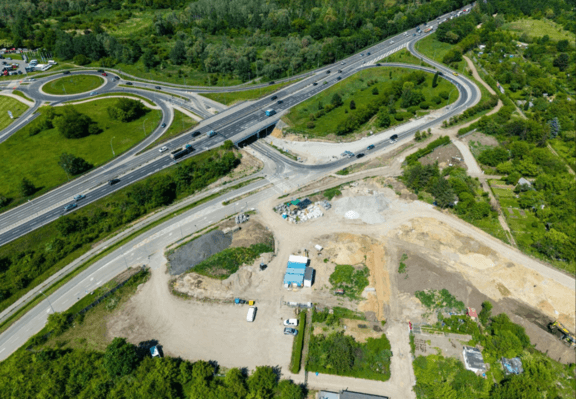 Budowa ostatniego odcinka Wschodniej Obwodnicy Wrocławia - rozbudowany węzeł drogowy ze zjazdami, rondem i wiaduktem, obok którego znajduje się otoczony zielenią plac budowy z ziemnymi wykopami i zapleczem technicznym