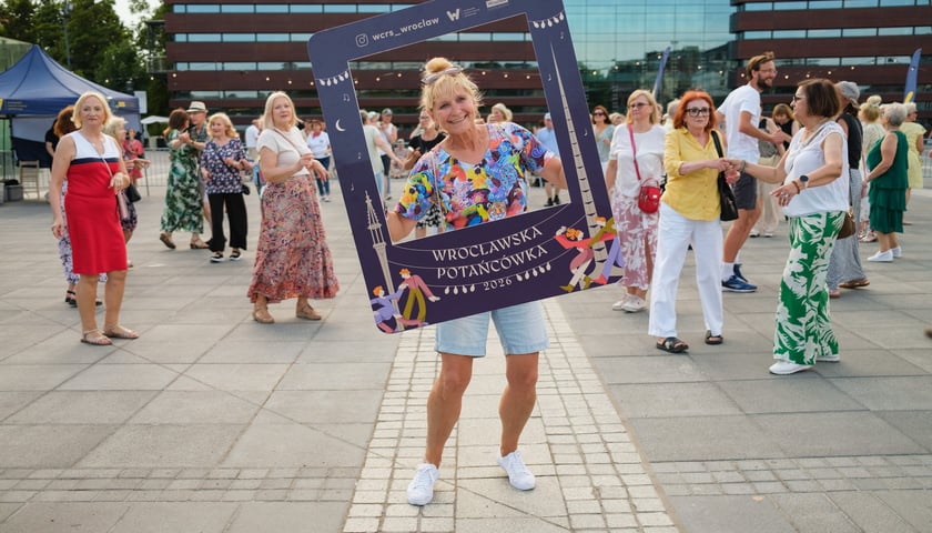Uśmiechnięta kobieta tańczy trzymając planszę z napisem 2026 / 19.06.2026 r.