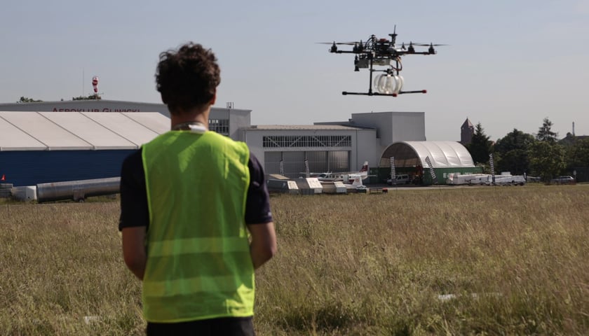 Mężczyzna w odblaskowej kamizelce steruje dronem.