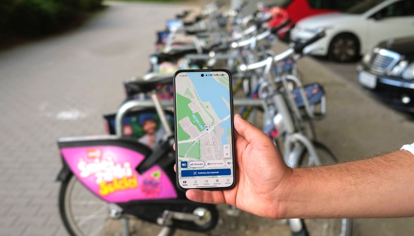 osoba pokazuje na ekranie telefonu mapę z lokalizacją stacji przy ul. Wejherowskiej, w tle zaparkowane rowery systemu WRM