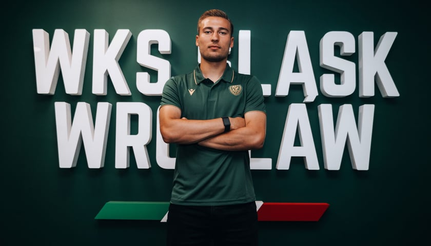 Mężczyzna stojący z założonymi rękami na tle napisu "WKS Śląsk Wrocław" - Dominik Szala, nowy piłkarz w klubie.