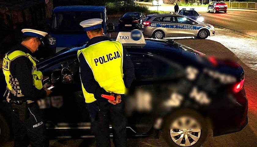 Policjanci kontrolują samochód z szyldem taxi. W tle radiowozy. Nocna akcja na Dolnym Śląsku. Taksówki na aplikację na celowniku służb 