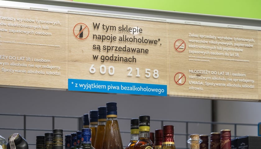 Półka z alkoholami w sklepie i tabliczka z informacją, że sprzedawane są w godzinach 6:00-21:58
