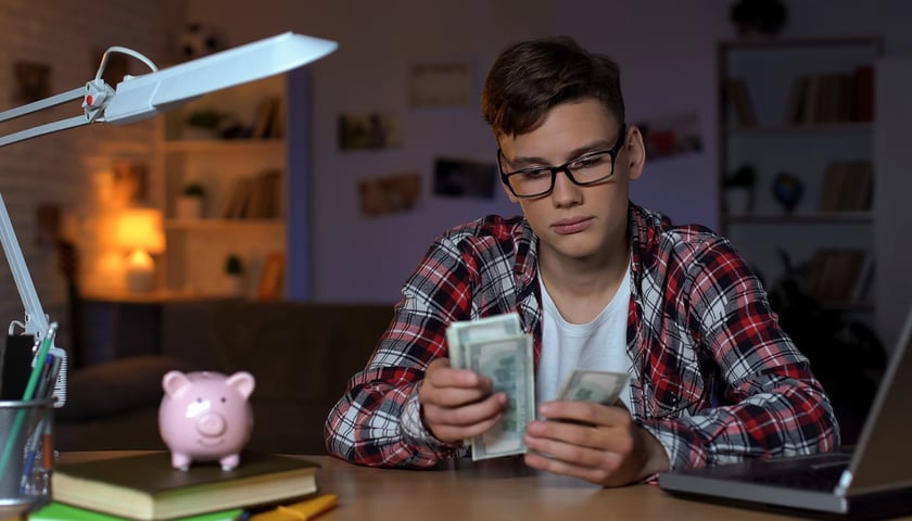 Na zdjęciu młody człowiek w okularach przelicza banknoty. Zdjęcie ilustracyjne