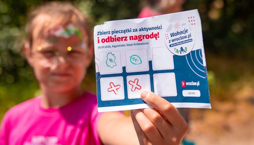 Chłopiec pokazuje kartkę służącą do zbierania pieczątek i zdobywania nagród. Zdjęcie z pikniku na Maślicach