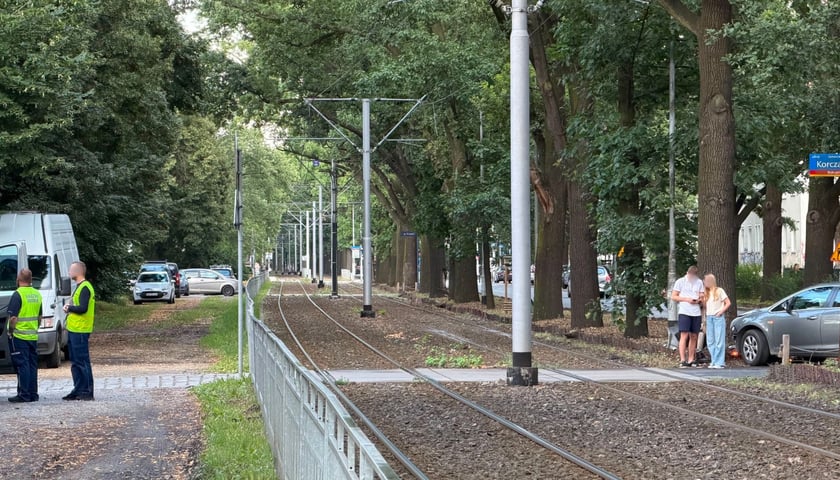 miejsce kolizji, z prawej strony widoczny jest rozbity samochód, z lewej pracownicy nadzoru ruchu MPK