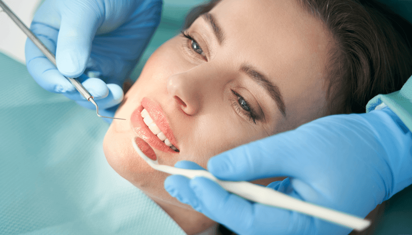 Uśmiechnięta pacjentka podczas rutynowego badania stomatologicznego wykonywanego przez dentystę w nowoczesnym gabinecie, zdjęcie ilustracyjne.