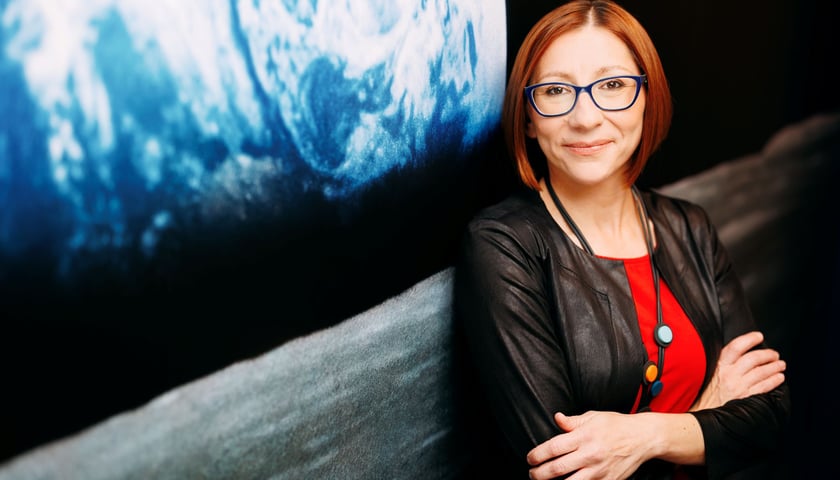 Kobieta stojąca przy zdjęciu Ziemi wykonanym z kosmosu - Anna Bukiewicz-Szul, koordynatorka programu ekranującego misji Ignis i współzałożycielka stowarzyszenia WroSpace.