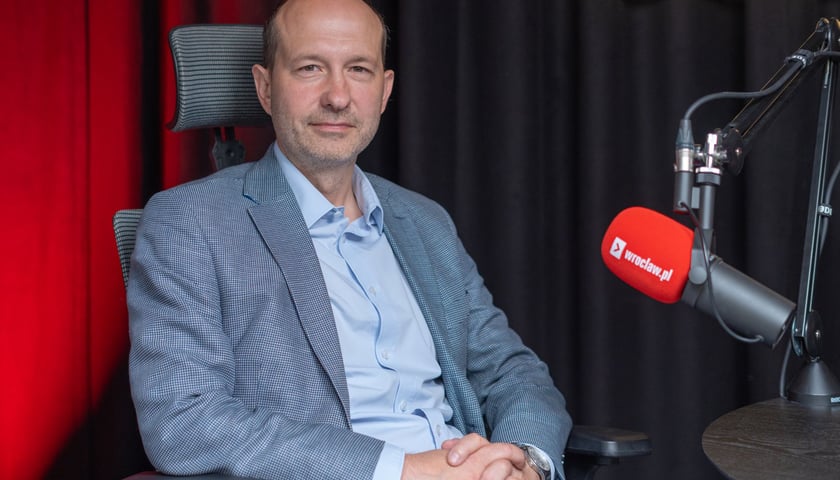 Mężczyzna w marynarce siedzący przy mikrofonie w studiu - Łukasz Kasztelowicz, radny miejski z klubu PiS.