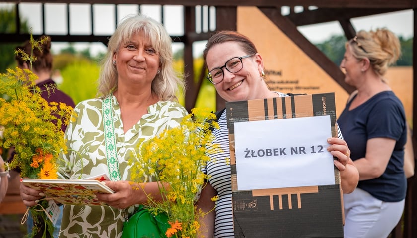 Dwie kobiety z dyplomami i kwiatami - jedna trzyma napis żłobek nr 12