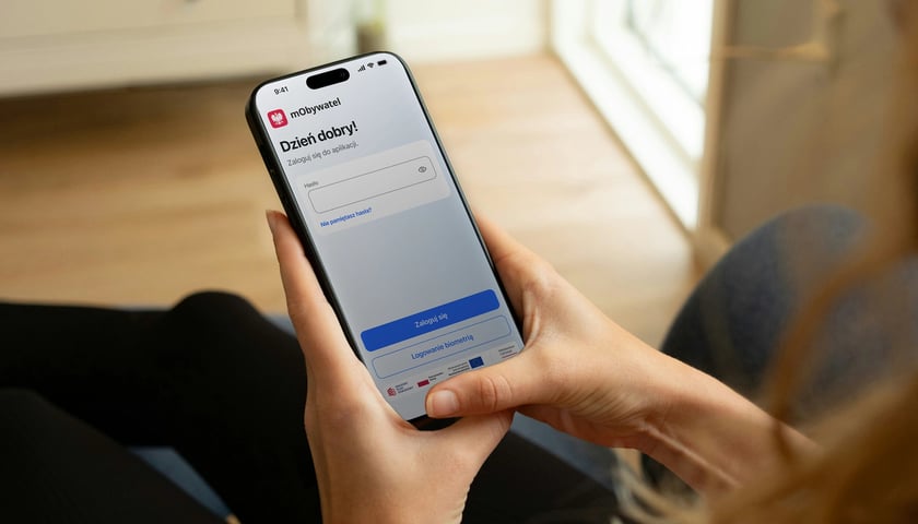 Smartfon z wyświetlonym ekranem aplikacji mObywatel, leżący w kobiecych dłoniach. Zdjęcie ilustracyjne.