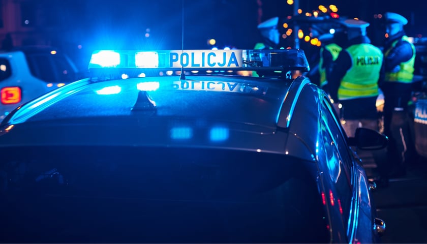 zdjęcie ilustracyjne: radiowóz policji, w tle grupa policjantów