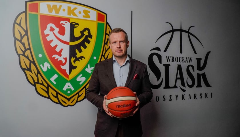 Michał Mazur trzymający piłkę przy ścianie z herbem Śląska i z logo klubu