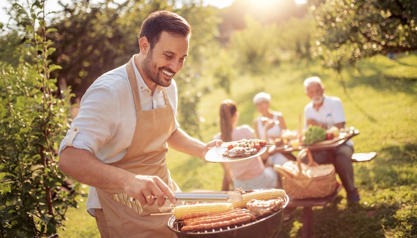 Grill z potrawami. Na zdjęciu uśmiechnięty mężczyzna obsługuje grilla
