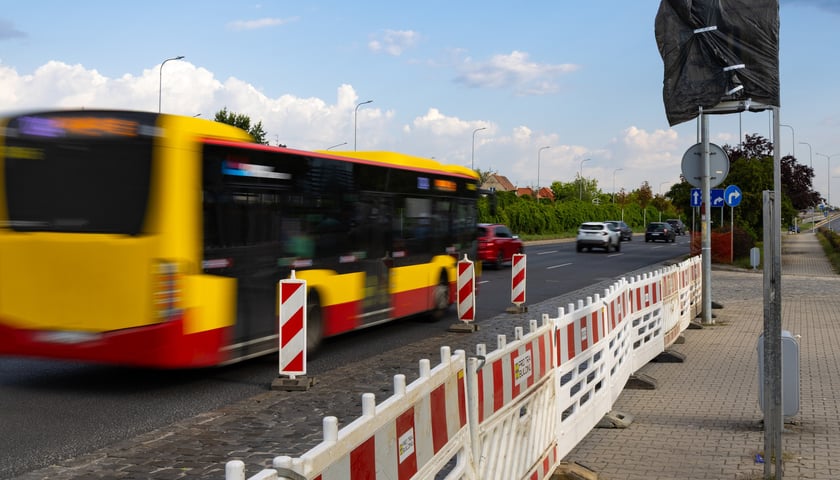 Wyłączony z ruchu przystanek z zasłoniętą tablicą i płotkami oddzielającymi od zatoki przy ul. Klecińskiej. Jezdnią przejeżdża autobus komunikacji miejskiej.
