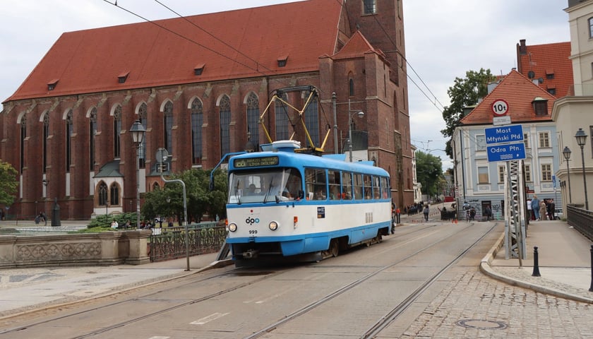 niebiesko-biały tramwaj Tatra T3 przejeżdża przez Most Młyński na Ostrowie Tumskim. W tle Kościół pw. NMP na Piasku