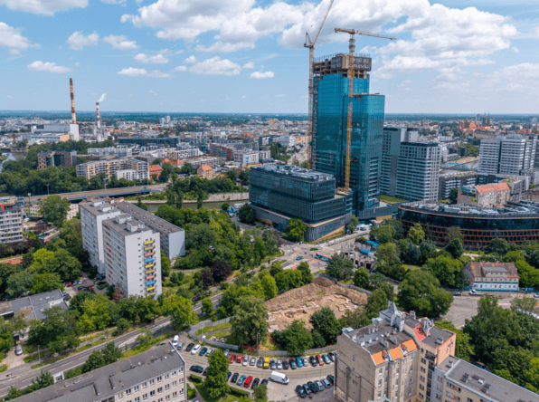 Widok z lotu ptaka na osiedle Szczepin z górującym nad nim nowoczesnym, przeszklonym wieżowcem w budowie i otaczającą go niższą zabudową, w tle - Nadodrze