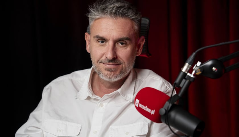 Mężczyzna w białej koszuli siedzi przy mikrofonie w studiu - Bartłomiej Ciążyński, radny miejski podczas nagrania podcastu Pytamy o Wrocław.