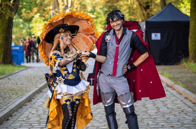 Para cosplayerów przebrana za Navia i Wriothesley z gry Genshin Impact, pozująca z uśmiechem na brukowanej alejce parkowej podczas wrocławskiego festiwalu Dni Fantastyki
