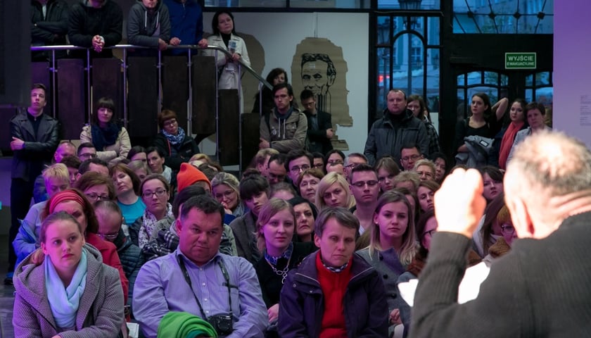 Publiczność zgromadzona we wnętrzu budynku podczas 12. edycji Europejskiej Nocy Literatury 2023 na osiedlu Huby, słuchająca prelegenta odwróconego tyłem do obiektywu