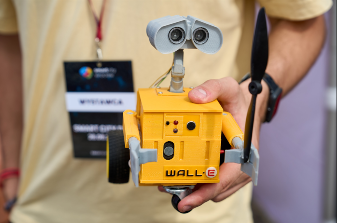 Robot przypominający postać Wall-E z filmu animowanego, trzymany w dłoni przez wystawcę podczas Smart City Day 2025