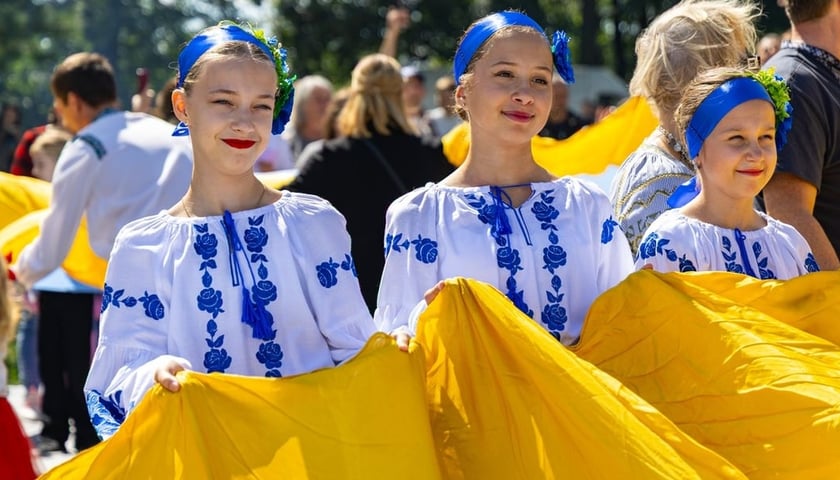 Три усміхнені дівчинки тримають у руках український прапор.  Міжкультурний пікнік з нагоди 35-ї річниці Незалежності України, 22.08.2026 р. 