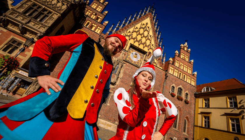 Dwoje ludzi przebranych za krasnoludków na tle wrocławskiego Ratusza