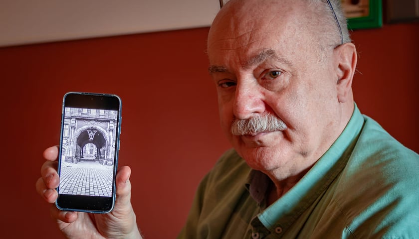 <p>Dr Maciej Łagiewski pokazujący na ekranie telefonu archiwalne zdjęcie bramy, w kt&oacute;rej wisiał szyld ze strzałką do synagogi.</p>