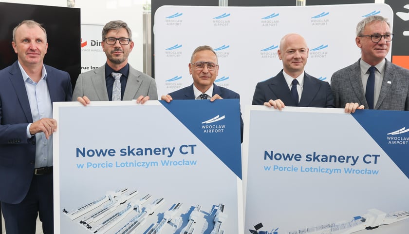 Piątka mężczyzn w garniturach trzymająca plansze z wizualizacjami linii w strefie kontroli bezpieczeństwa na lotnisku we Wrocławiu, 7 września 2026. Od lewej: Marcin Janusz (Anglosec), Błażej Nowakowski (Dimark), Cezary Pacamaj, Karol Przywara i Dariusz Kowalczk