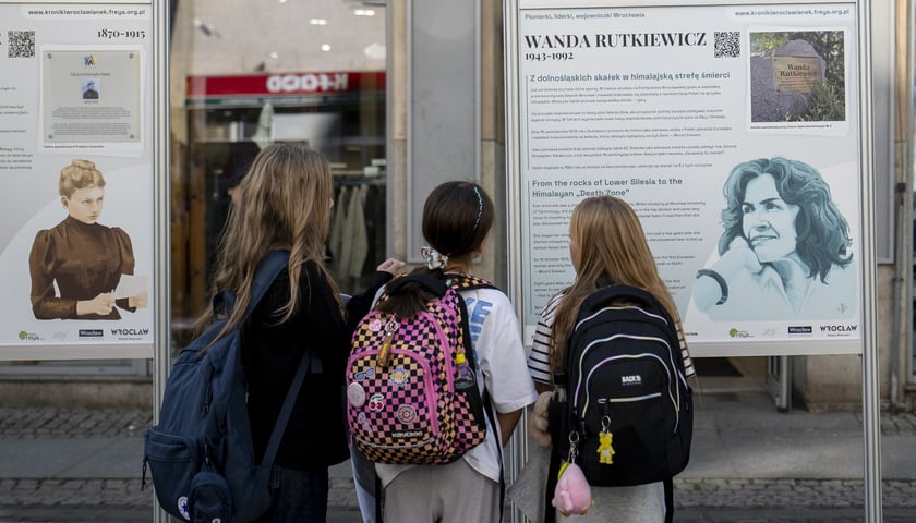 Trzy dziewczynki w wieku szkolnym oglądają wystawę "Kroniki Wrocławianek" na ulicy Oławskiej