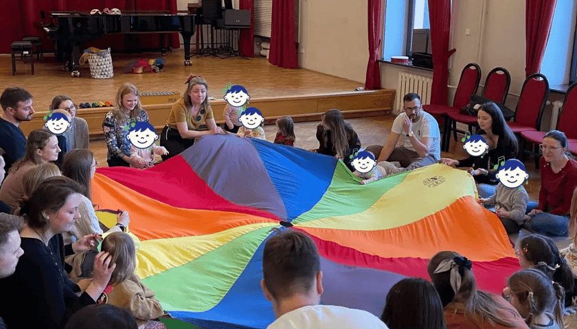 Zdjęcie z zeszłorocznych zajęć. Opiekunowie i ich dzieci uczestniczą we wspólnej zabawie w ramach zajęć.