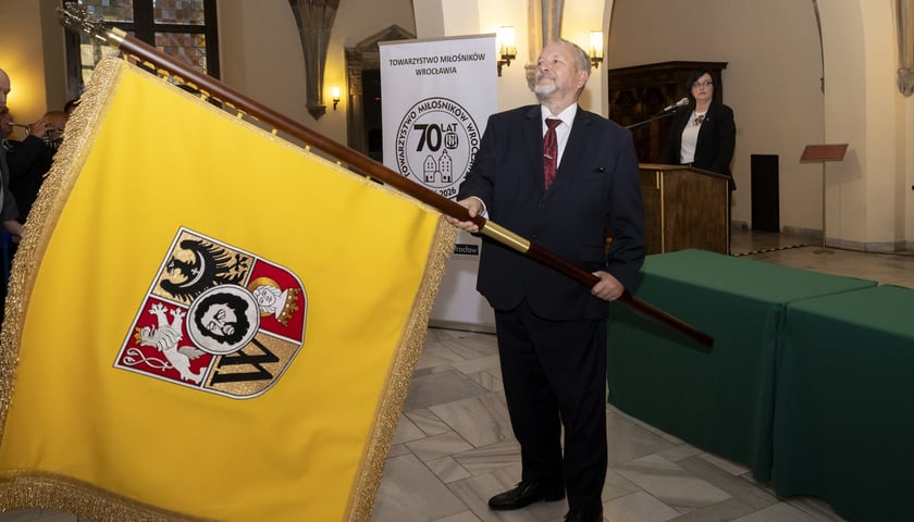 Mężczyzna w garniturze trzymający sztandar z herbem Wrocławia - Towarzystwo Miłośników Wrocławia odbiera własny sztandar podczas uroczystości z okazji 70-lecia istnienia, 23 września 2026 r.