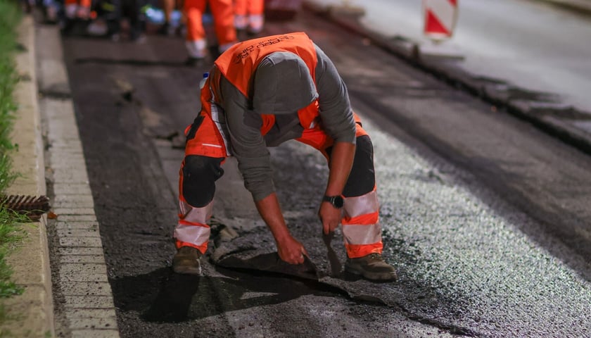 Robotnik pochylony nad asfaltem Alei Hallera podczas wieczornych prac remontowych