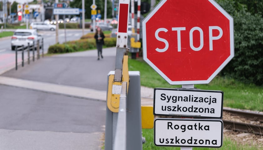 Znak STOP z tabliczkami „Sygnalizacja uszkodzona” i „Rogatka uszkodzona” stoi przy podniesionej rogatce na przejeździe kolejowym, a w tle widać ulicę z samochodami. Uszkodzone rogatki na przejeździe przy ul. Strzegomskiej.