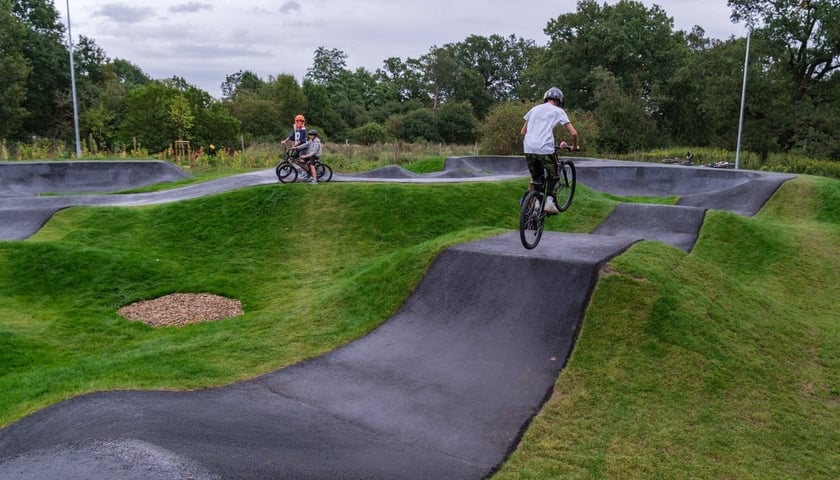 Trójka młodych ludzi na rowerach jeździ po pumptracku przy ulicy Jajczarskiej