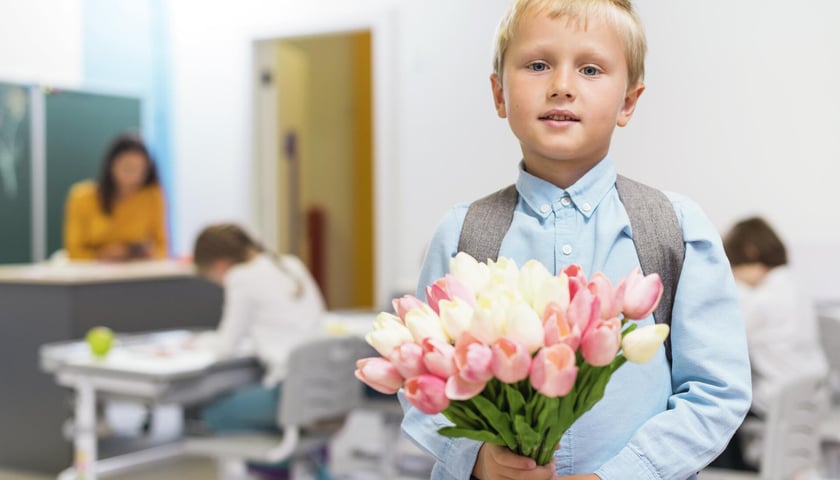 Uczeń z kwiatami dla nauczyciela. Jakie inne prezenty można wręczyć wychowawcy na zakończenie roku szkolnego?
