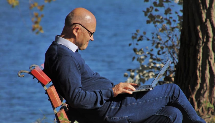 senior korzystający z laptopa na ławce w parku, zdjęcie ilustracyjne