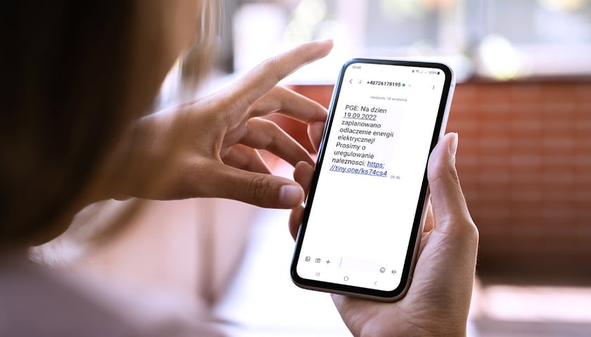 Na zdjęciu: osoba odczytująca SMS, którym napisano: „PGE: na dzień 19.09.2022 zaplanowano odłączenie energii elektrycznej ! Prosimy o uregulowanie należności”