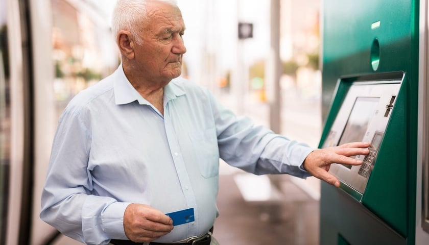 Na zdjęci jest starszy mężczyzna wypłacający pieniądze z bankomatu, zdjęcie ilustracyjne 