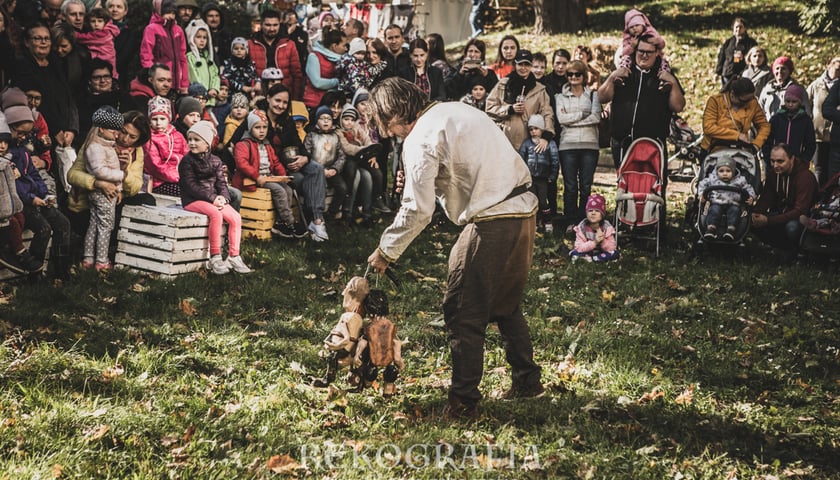 Na zdjęciu tłum dzieci przygląda się kuglarzowi z marionetkami występującemu na trawie