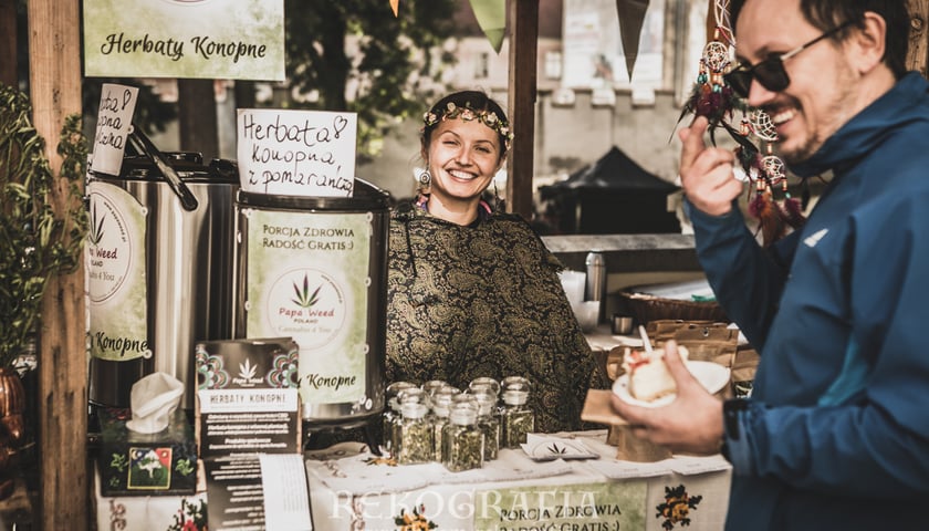Na zdjęciu kram na jarmarku z uśmiechniętą ekspedientką i kupującym mężczyzną