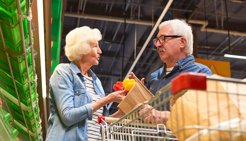 Na zdjęciu widać parę seniorów - kobietę i mężczyznę - która robi zakupy w sklepie. 