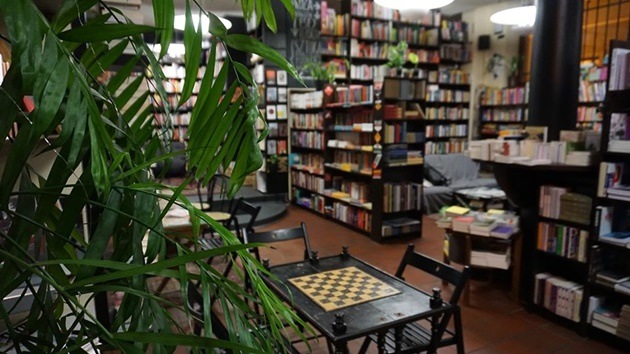 Na zdjęciu wnętrze Café księgarnia Tajne Komplety, na pierwszym planie kwiatek, w  głębi półki z książkami